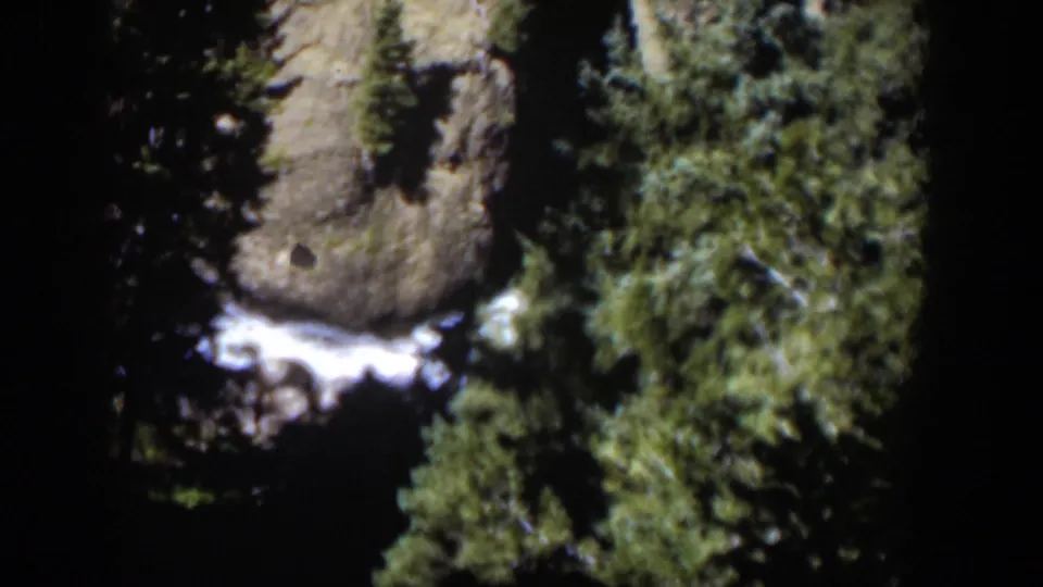 1951 Wyoming 8mm frame of a rocky forest canyon with white rushing water visible below evergreen branches.