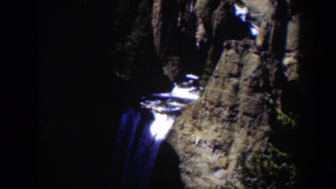Waterfall dropping through dark rocky canyon walls with bright highlights on the water.