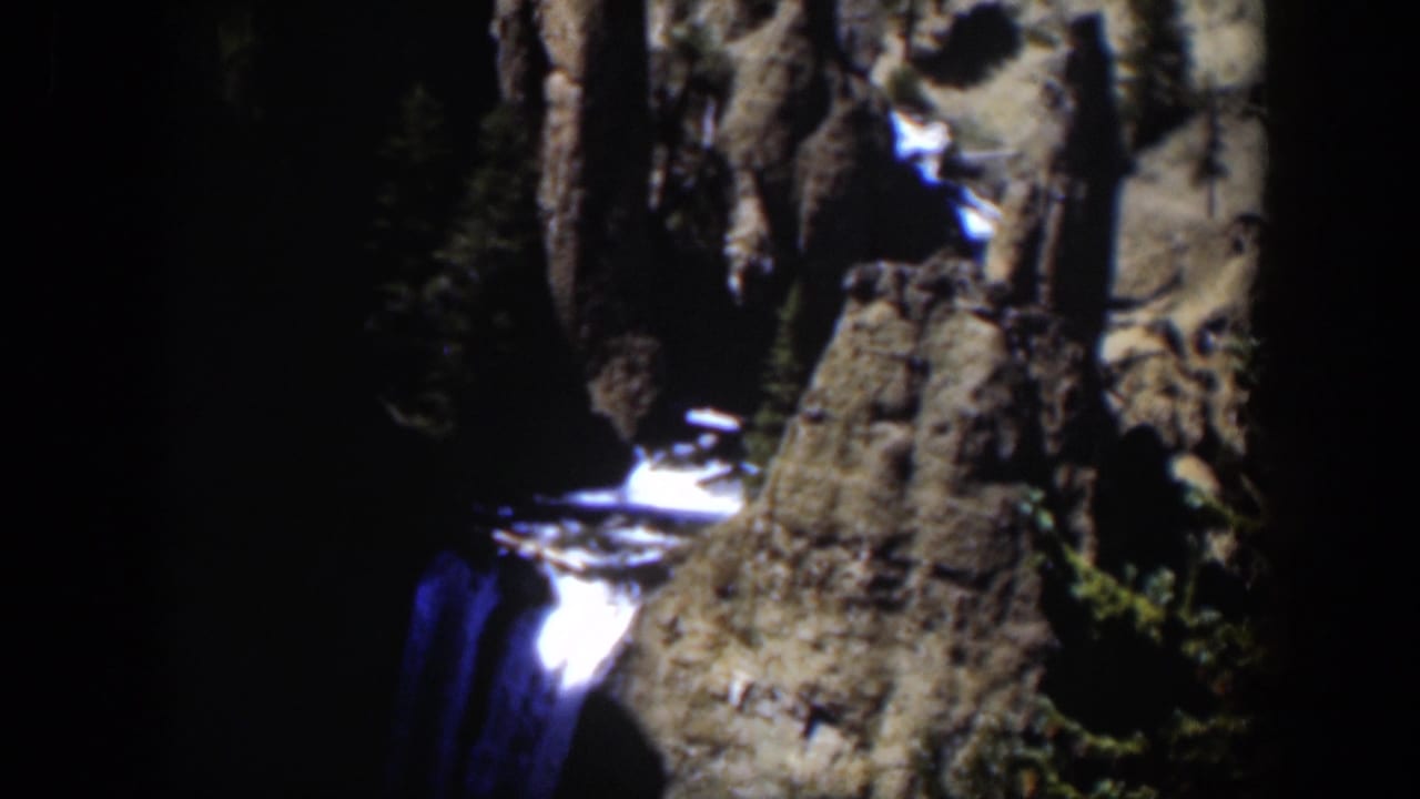 1951 Wyoming home-movie frame of a rocky canyon face with a small bright waterfall in deep shadow.