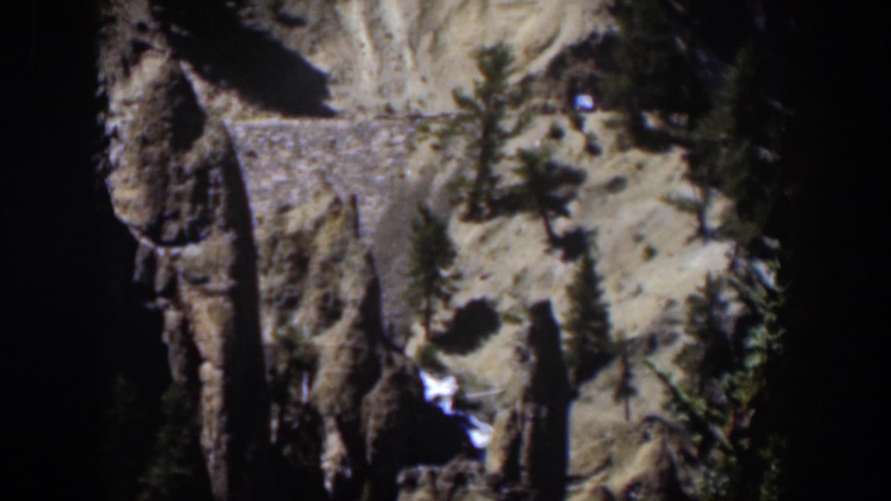 Rocky canyon slope with evergreen trees and a horizontal stone wall.