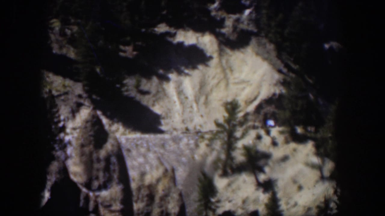 Rocky mountain slope with dark evergreen shadows and pale snow or exposed ground.