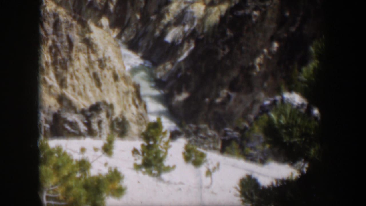 1951 Wyoming 8mm frame showing a steep pale mountain cut or ravine, dark rock walls, and evergreen trees near the base.