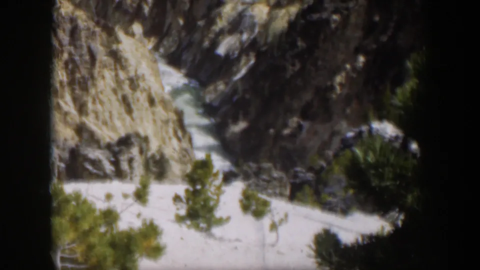 1951 Wyoming 8mm frame showing a steep pale mountain cut or ravine, dark rock walls, and evergreen trees near the base.
