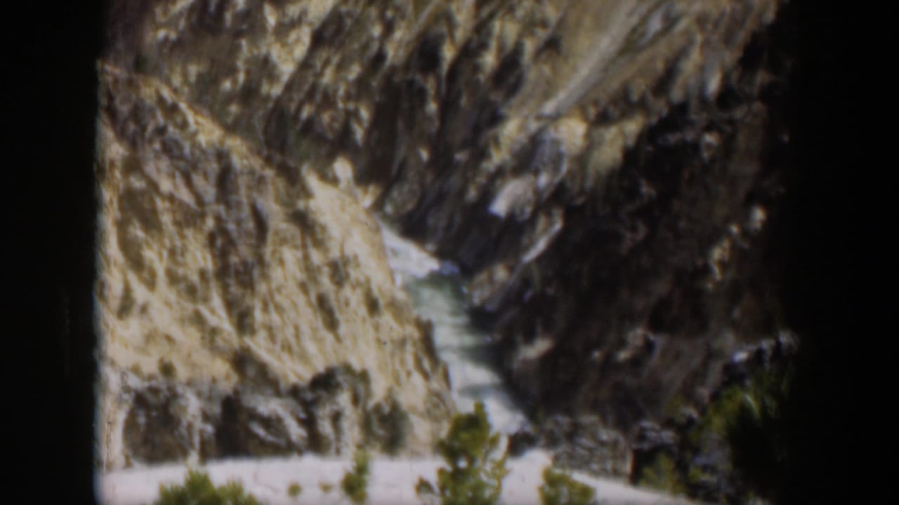 Wyoming 1951 8mm frame showing a rugged gorge, narrow watercourse, rocky slopes, and small evergreens in soft home-movie focus.