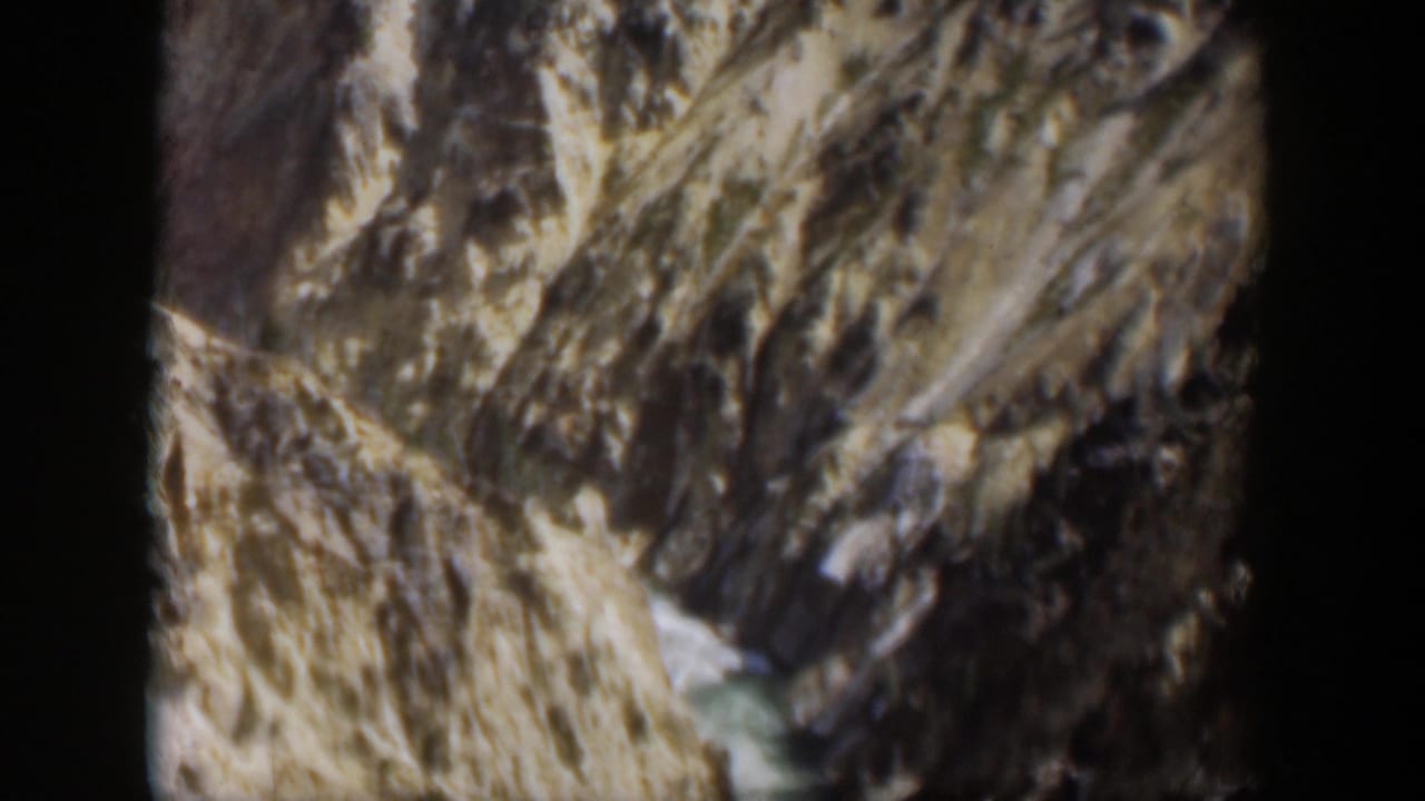 1951 Wyoming 8mm frame showing steep rock faces and a small stream through a rugged mountain valley.