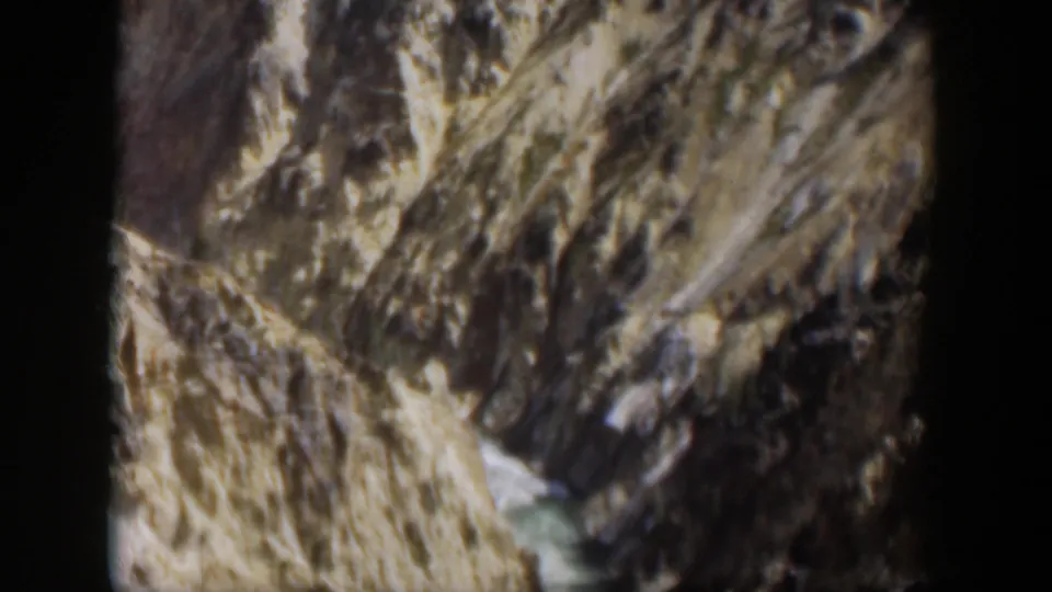 1951 Wyoming 8mm frame showing steep rock faces and a small stream through a rugged mountain valley.