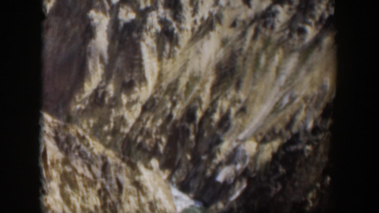 1951 Wyoming home-movie frame of textured rock walls and pale landslide-like slopes in a mountain park setting.