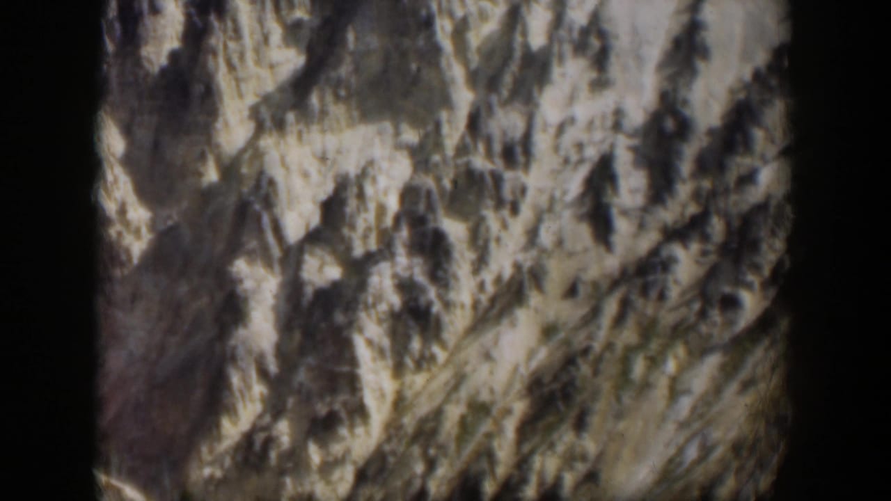 Rocky mountain slope with pale snow or light rock patches and dark film borders.