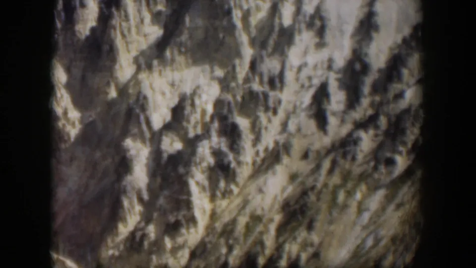 1951 Wyoming 8mm frame showing a rugged rocky mountainside with pale patches and shadowed textures.
