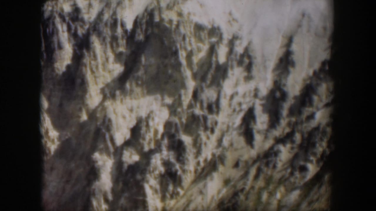 1951 Wyoming 8mm frame of a steep, textured mountain face with bright pale areas and darker ridges.