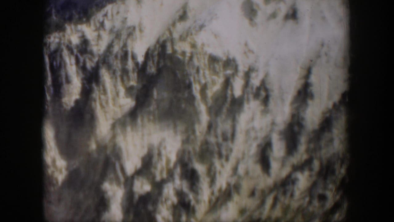 1951 Wyoming 8mm frame showing a rugged slope with pale high areas and dark striated rock.