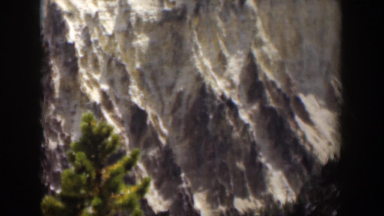 1951 Wyoming 8mm frame with pale cliff rock, dark vertical film edge, and a foreground evergreen.