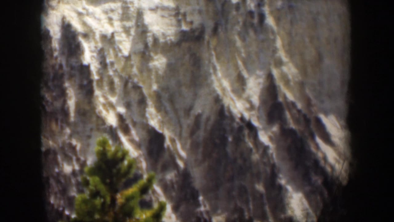 1951 Wyoming home-movie frame showing textured mountain rock and a blurred evergreen foreground.