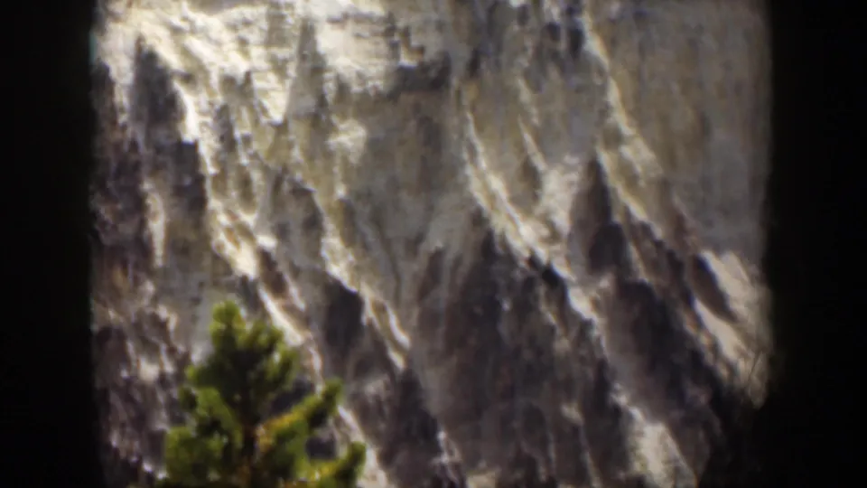 1951 Wyoming home-movie frame showing textured mountain rock and a blurred evergreen foreground.