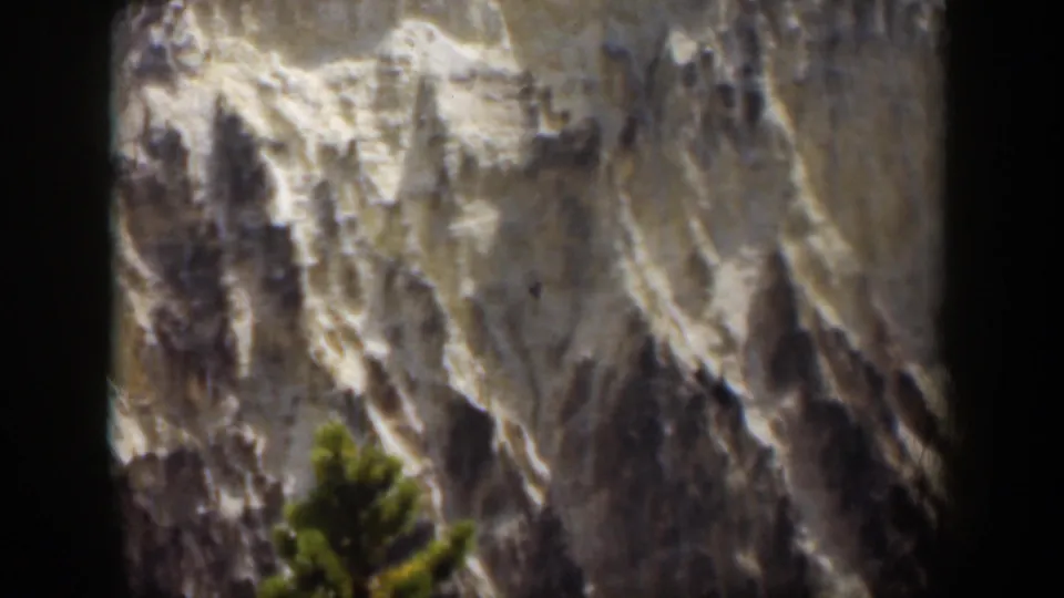 1951 Wyoming 8mm frame of a rugged rock face with a foreground evergreen and visible film borders.