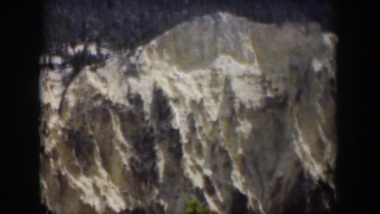 1951 Wyoming 8mm view of a pale mountain shoulder with snow streaks, dark treeline at the top, and soft home-movie texture.