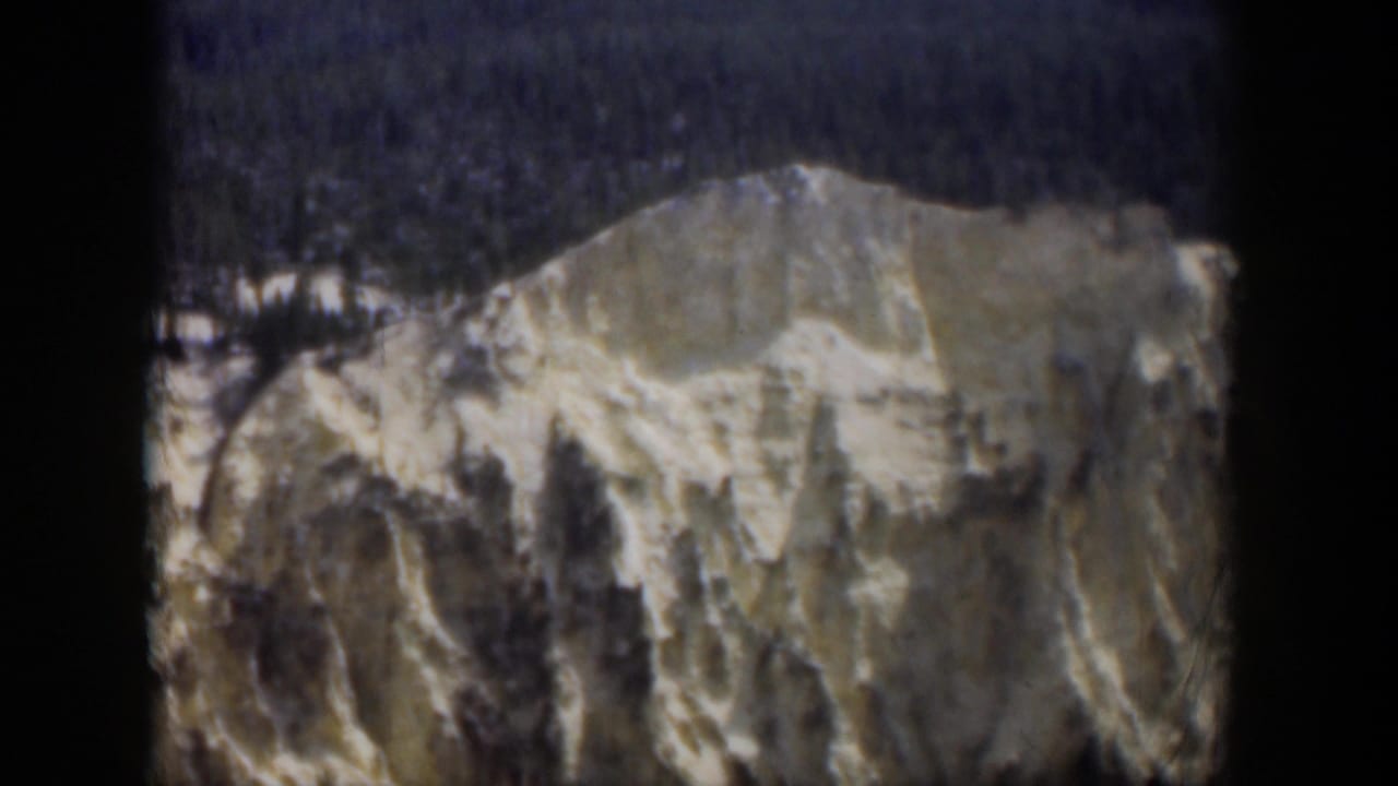 1951 Wyoming frame showing a pale rocky ridge, scattered snow markings, dark trees above, and 8mm gate-edge borders.