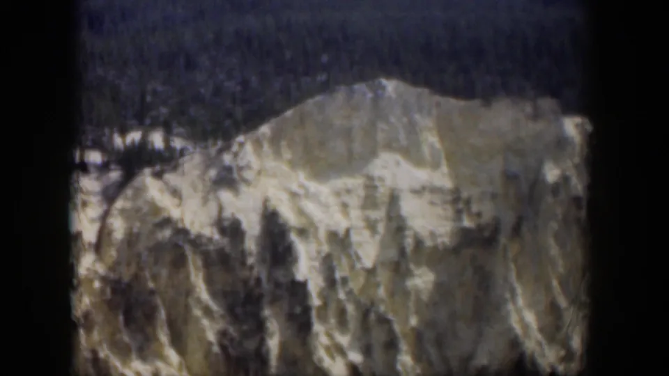 1951 Wyoming frame showing a pale rocky ridge, scattered snow markings, dark trees above, and 8mm gate-edge borders.