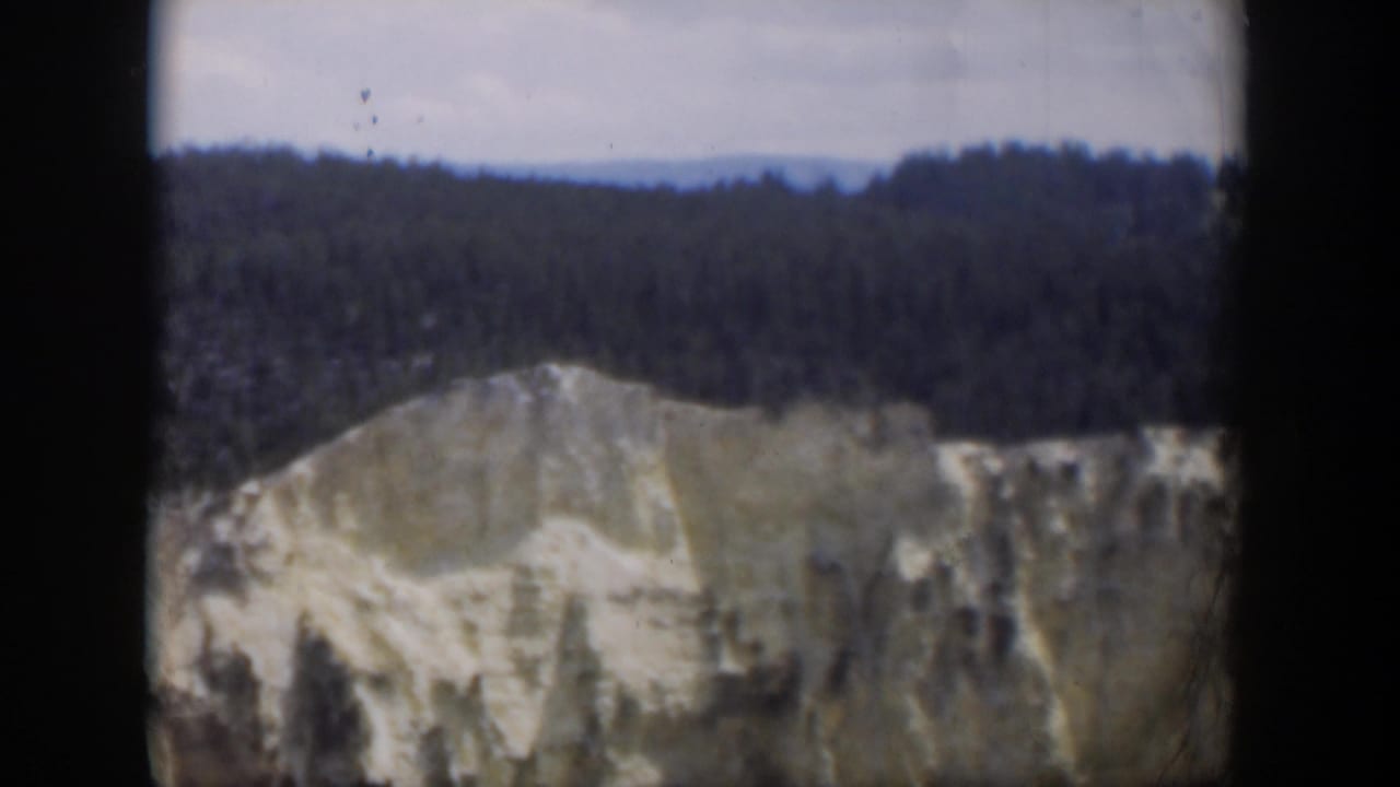 1951 Wyoming home-movie frame with a soft, grainy close view of a pale cliff face below forested hills.