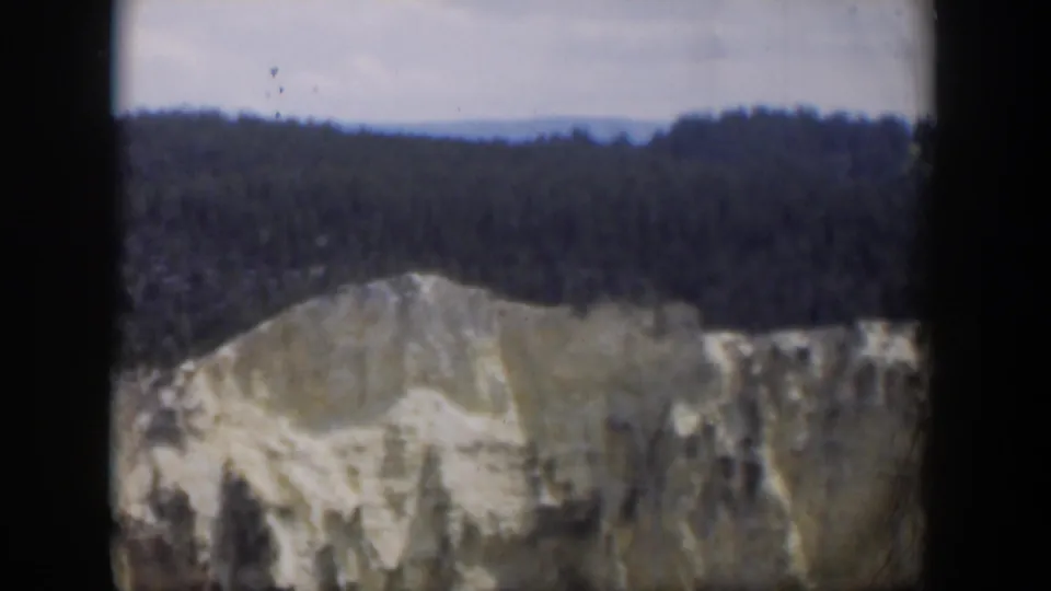 1951 Wyoming home-movie frame with a soft, grainy close view of a pale cliff face below forested hills.