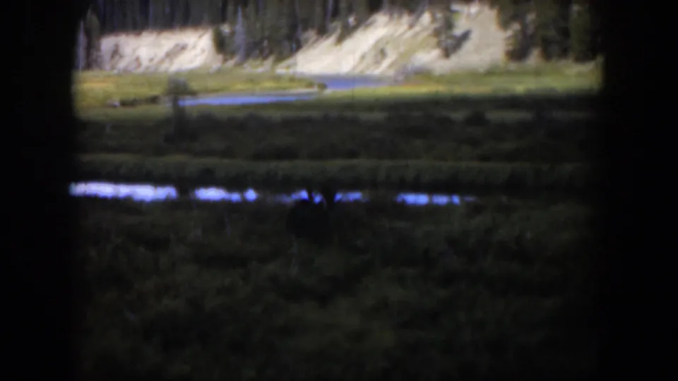1951 Wyoming 8mm frame revealing a green valley, reflective stream or pond, pale cliffs, and scattered trees.
