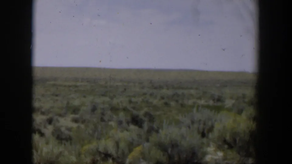 Wyoming landscape frame showing a broad sagebrush field, distant flat horizon, pale sky, and visible 8mm gate edges.