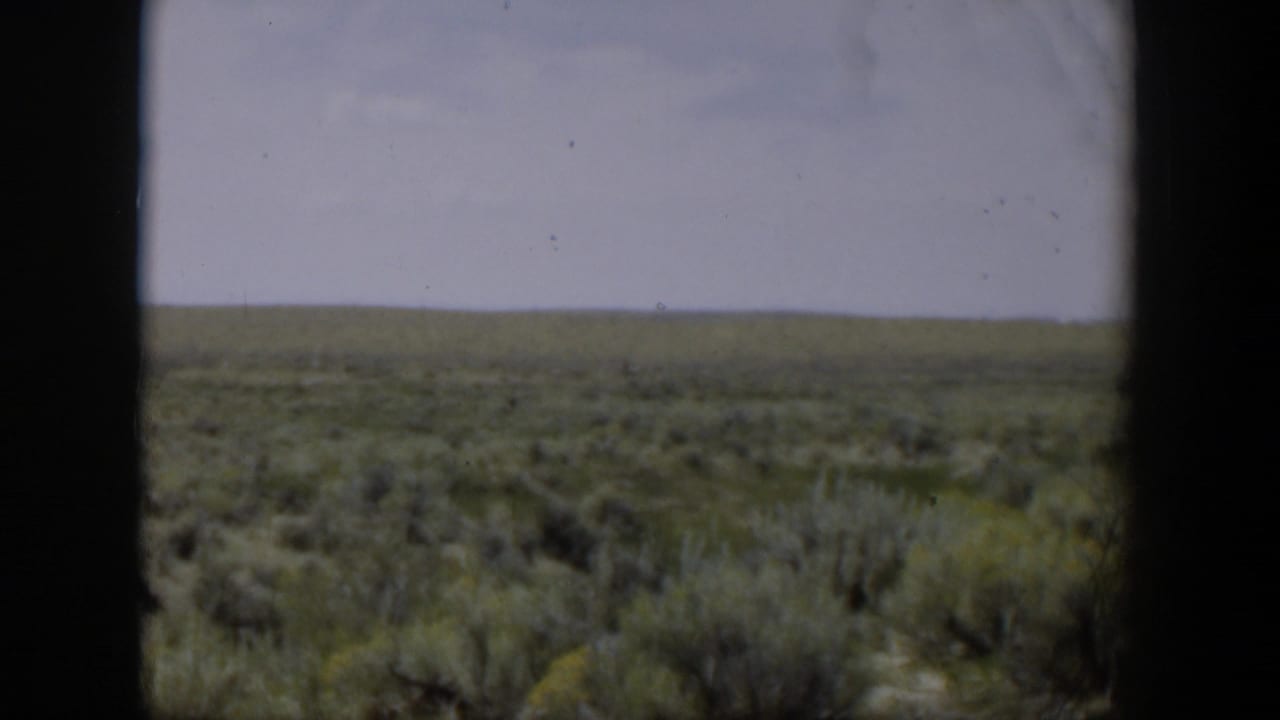 1951 Wyoming scrubland viewed through a dark window frame, with a flat horizon and pale sky.