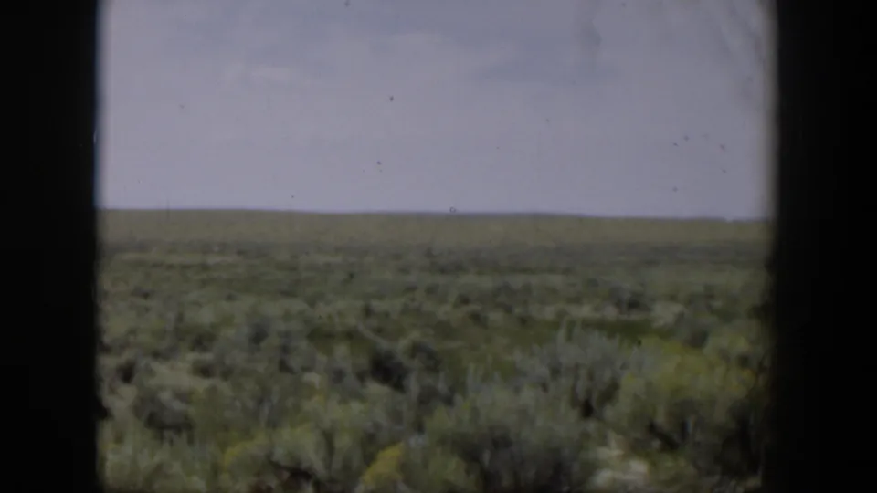 1951 Wyoming scrubland viewed through a dark window frame, with a flat horizon and pale sky.