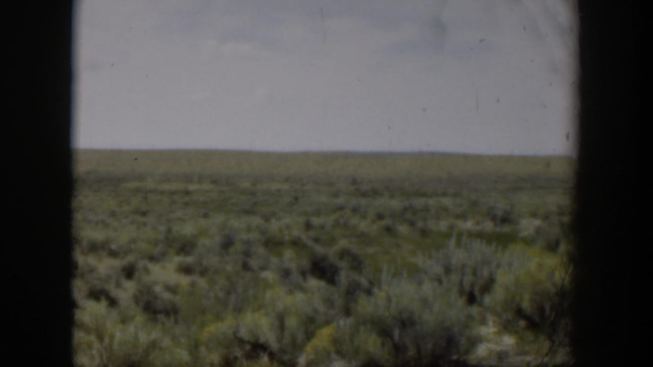 1951 Wyoming arid landscape with low brush, pale sky, and heavy dark frame edges from the filming position.