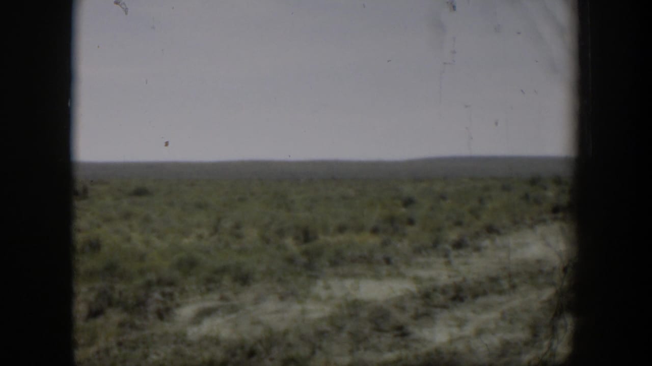 Wyoming scrubland home-movie view from 1951, with dry ground, low brush, and a broad pale sky.