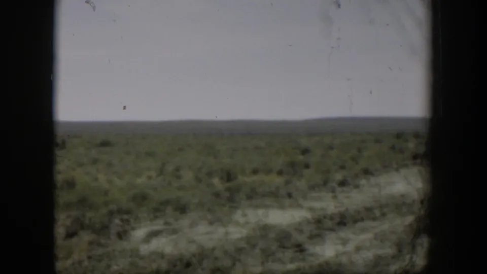 Wyoming scrubland home-movie view from 1951, with dry ground, low brush, and a broad pale sky.