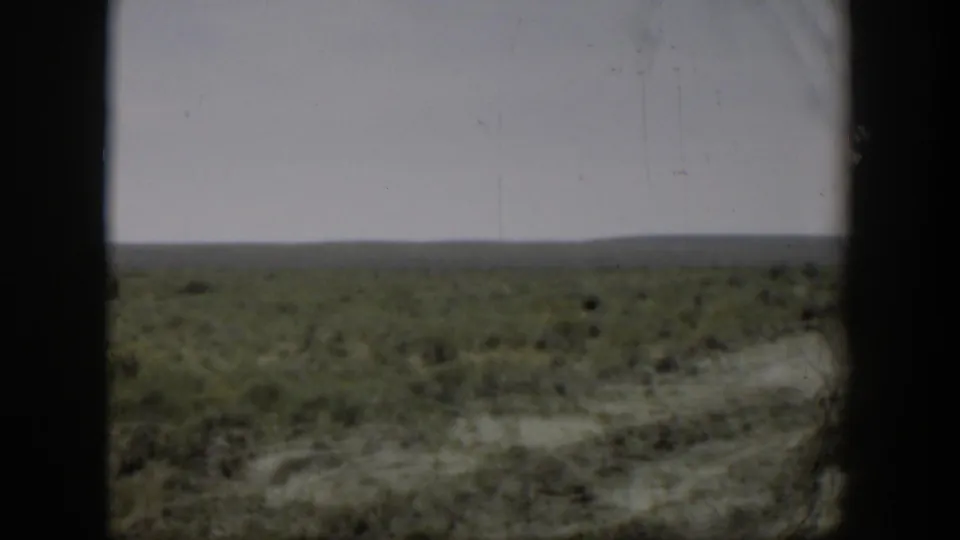 1951 Wyoming 8mm home-movie frame showing low vegetation and pale soil stretching to a flat horizon under an overcast sky.