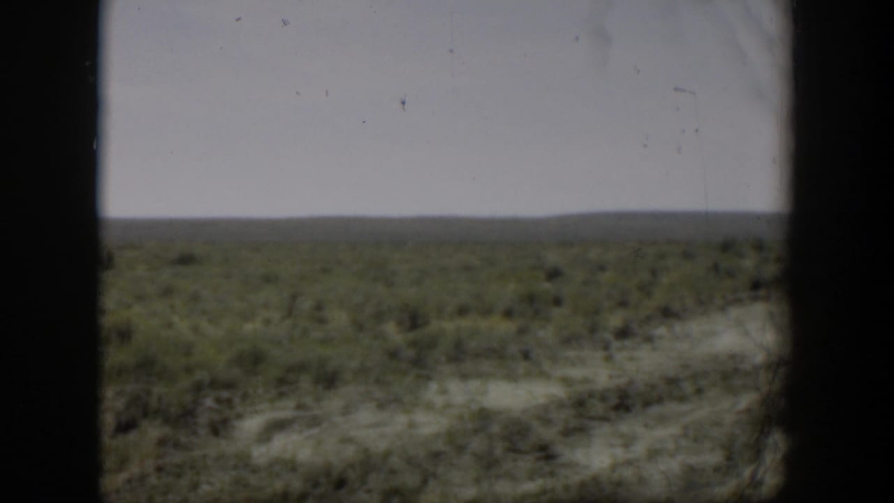 1951 Wyoming home-movie still of open rural land with low vegetation and a distant horizon under muted, cloudy light.