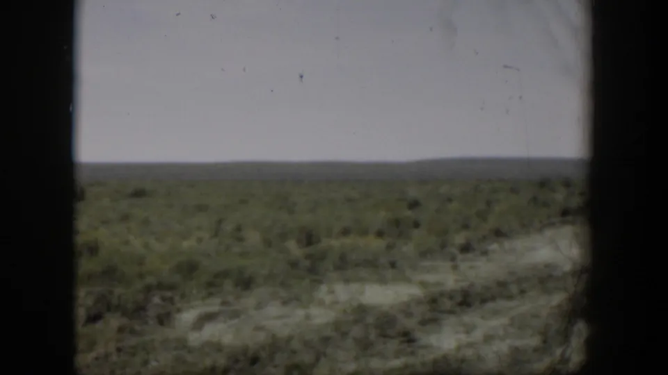 1951 Wyoming home-movie still of open rural land with low vegetation and a distant horizon under muted, cloudy light.
