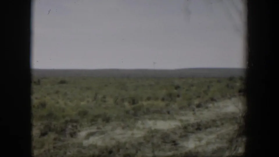 1951 Wyoming 8mm frame showing low arid scrubland and distant horizon viewed through dark window-like borders.
