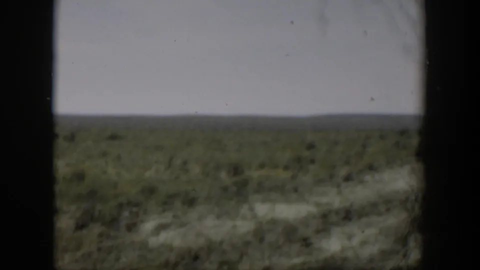 Soft 8mm view of Wyoming scrub and distant low hills, with dark borders suggesting a window or film gate edge.