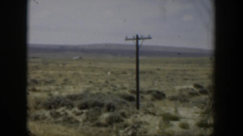 Soft 8mm Wyoming view of a utility pole with wires crossing open arid ground and low distant hills.