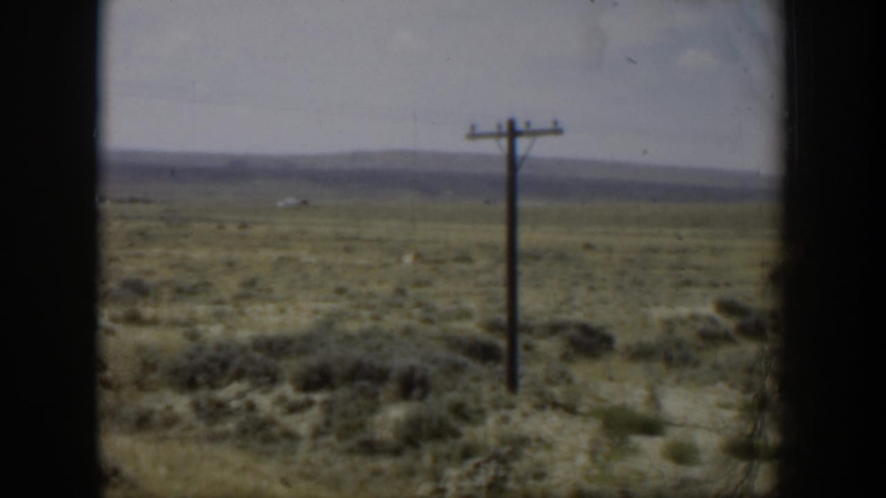 1951 Wyoming 8mm frame with open brush, a foreground utility pole, distant mountain ridge, and soft home-movie color.