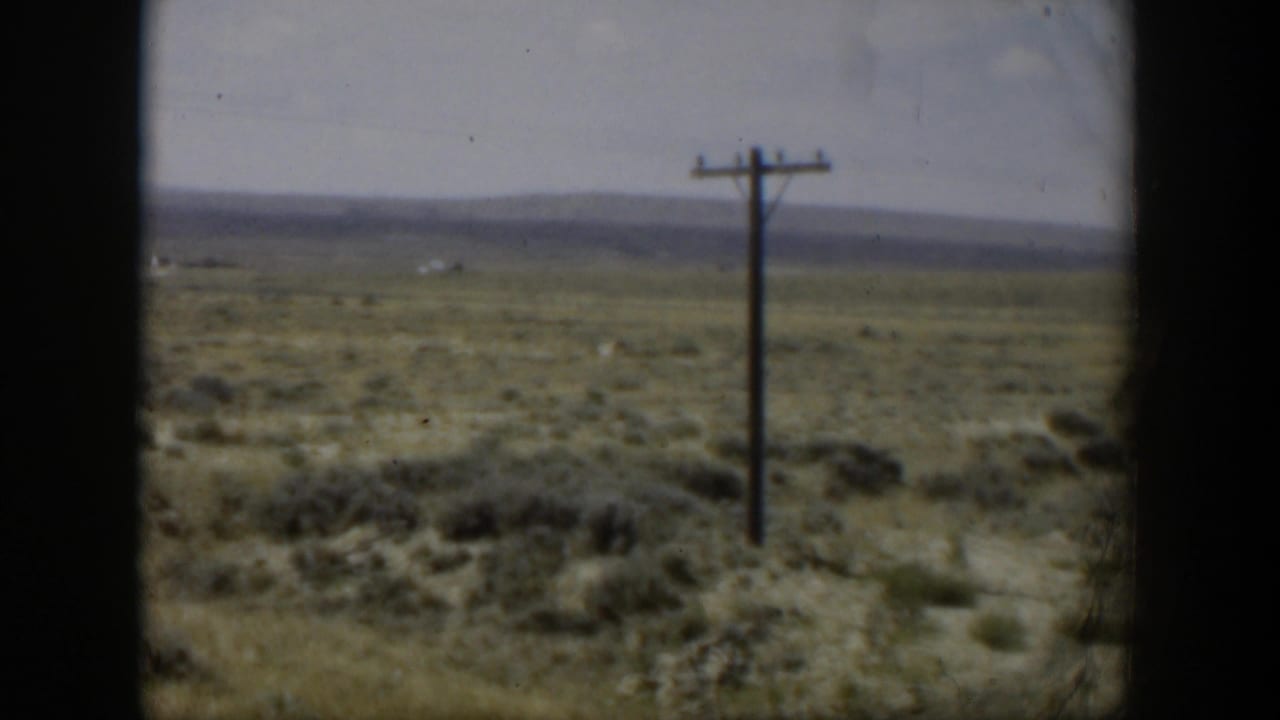 Dry scrubland with a wooden utility pole, distant hills, pale sky, and dark film borders.