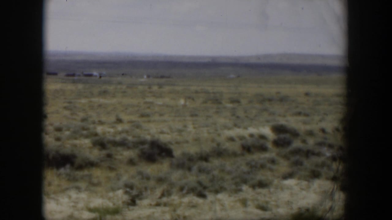 1951 Wyoming 8mm frame looking across dry scrubland toward faint structures and low hills, bordered by dark film or window edges.