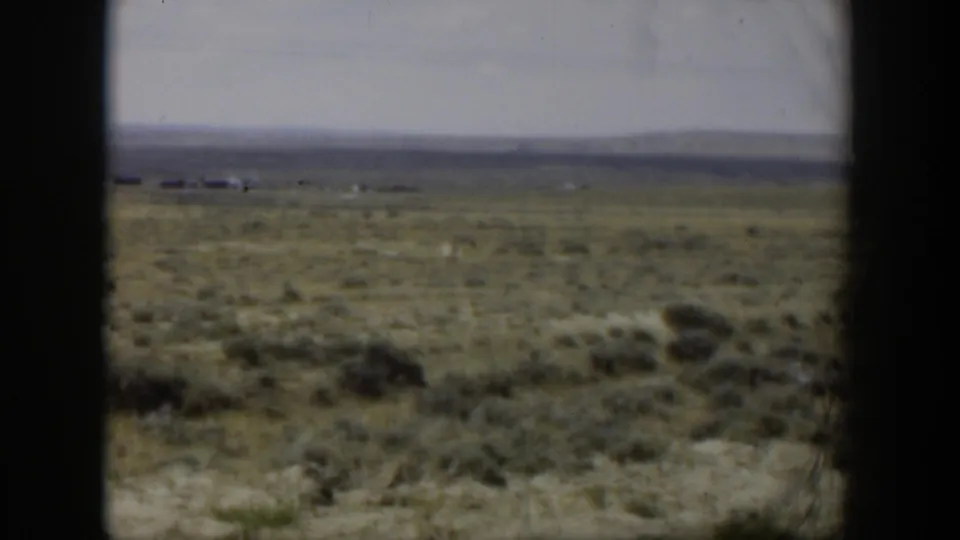 1951 Wyoming 8mm frame looking across dry scrubland toward faint structures and low hills, bordered by dark film or window edges.