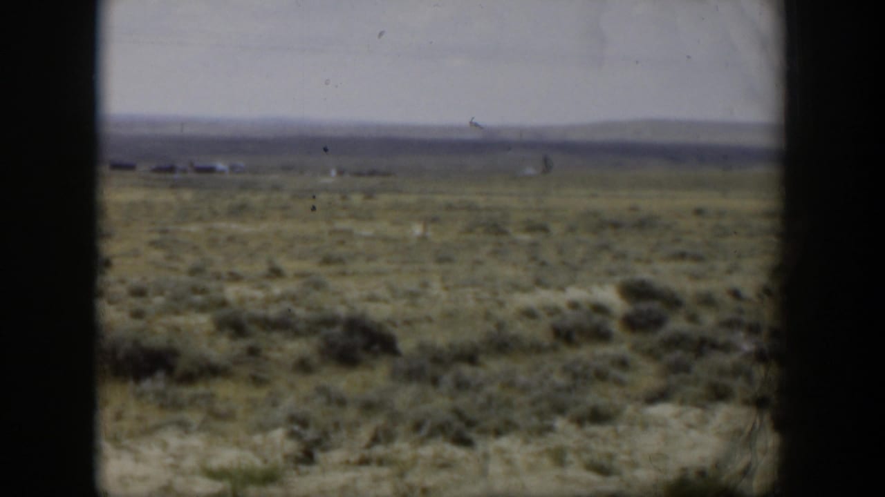 1951 Wyoming 8mm frame of open scrubland with faint horizon buildings or structures, low hills, and soft film grain.