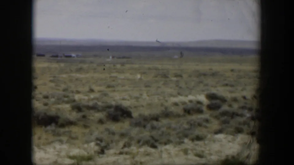 1951 Wyoming 8mm frame of open scrubland with faint horizon buildings or structures, low hills, and soft film grain.