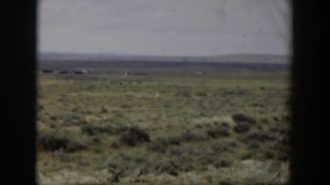 Distant deer running through a broad Wyoming sagebrush field in a soft, faded 1951 8mm home-movie frame.