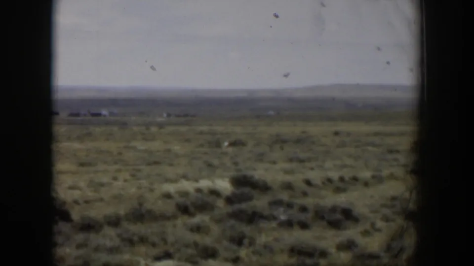 1951 Wyoming home-movie still with open rangeland, distant horizon, and a small deer moving through sagebrush.