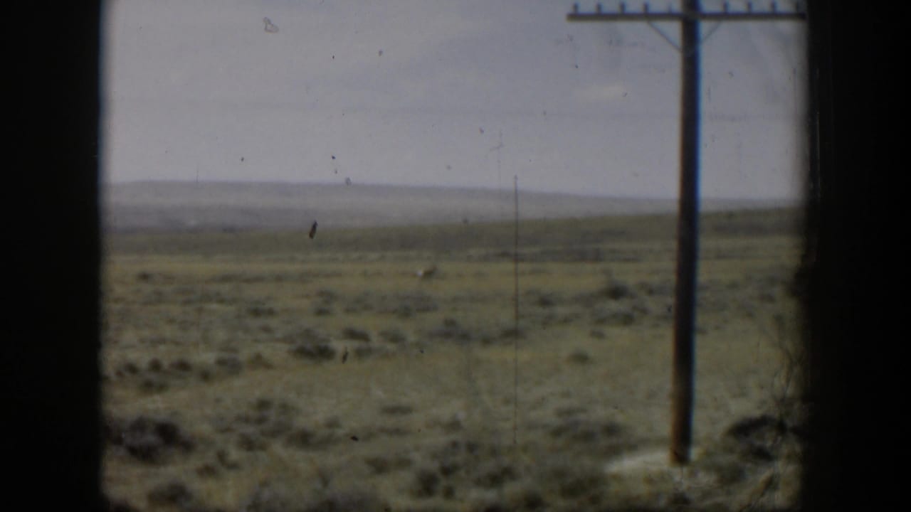 1951 Wyoming 8mm frame showing open grassland through a dark window frame, with a utility pole and a low distant horizon.