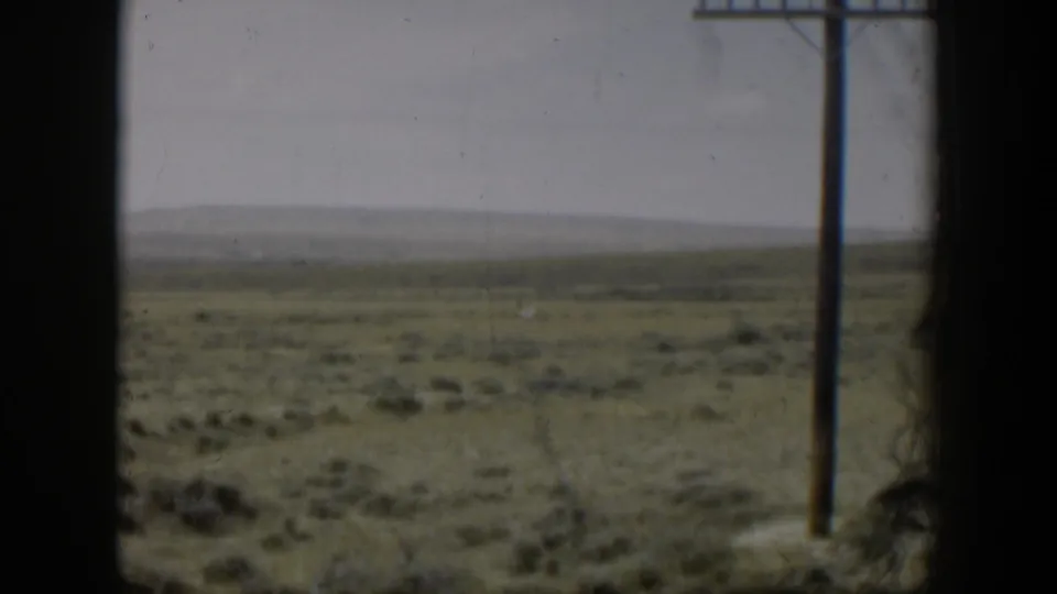 1951 Wyoming home-movie frame of open plains seen through a window, with a right-side utility pole and hazy horizon.