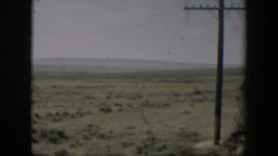 1951 Wyoming home-movie view of open plains and a utility pole from a moving vehicle, with dark window or film gate edges.