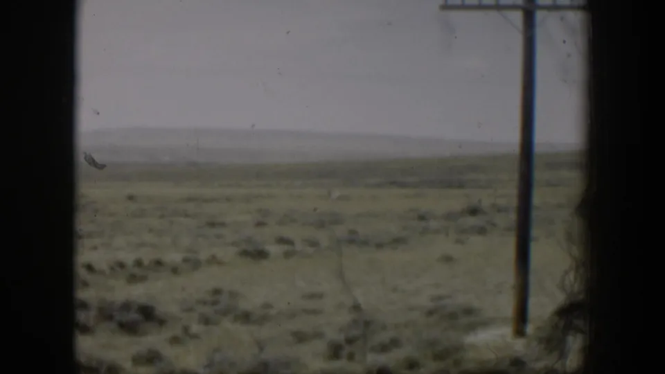 Open Wyoming plains from a moving vehicle, with a wooden utility pole and muted 8mm color visible through dark frame edges.