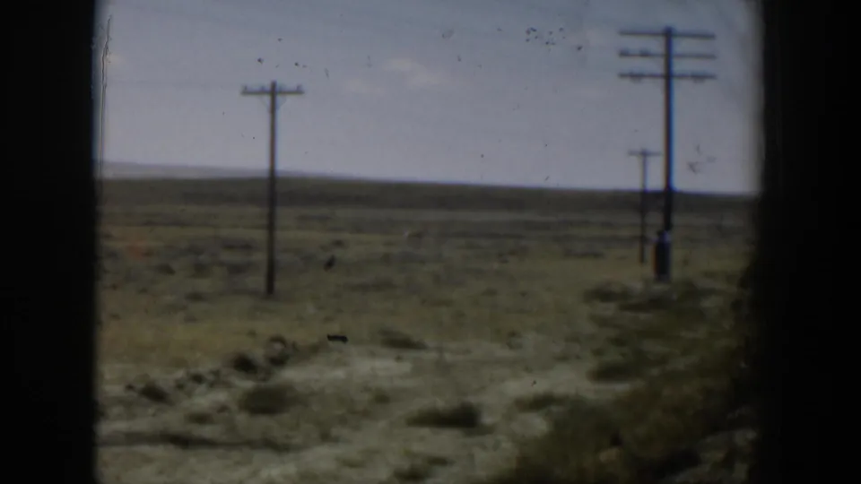 1951 Wyoming plains view with multiple wooden utility poles receding into the distance across dry grass and sagebrush.